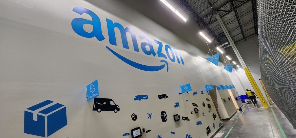 Inside the Amazon warehouse, the vast company logo dominates the wall, complemented by icons of packages and vehicles. As part of their innovative SSD program, efficiency soars with every detail meticulously designed for optimal performance.