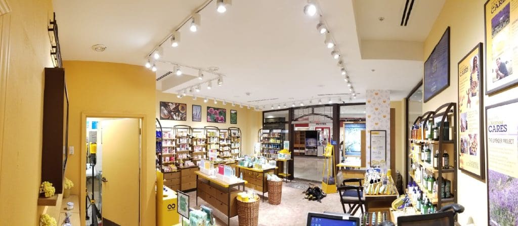 A well-lit shop interior in Roseville features wooden shelves displaying various products. Baskets and items are arranged neatly in the center. The upgraded yellow walls create a warm ambiance, with the doorway visible in the background.