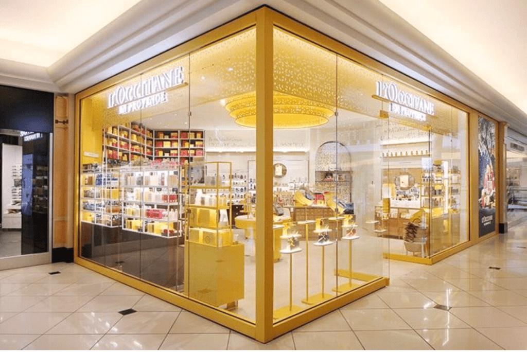 The elegantly illuminated storefront of L'Occitane en Provence at Somerset Collection showcases an opulent chandelier and well-stocked shelves, nestled among luxury retailers in the vibrant shopping mall.