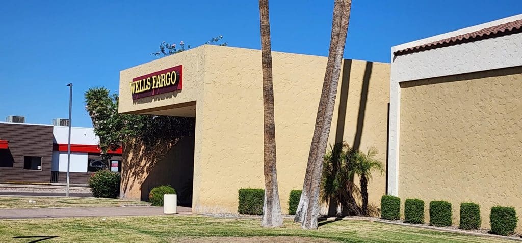 A Wells Fargo bank branch with a beige exterior and a red and yellow sign is shown, seamlessly integrated into the surroundings as if part of a TEST FIT program. Palm trees and trimmed hedges add to its inviting presence in the community.