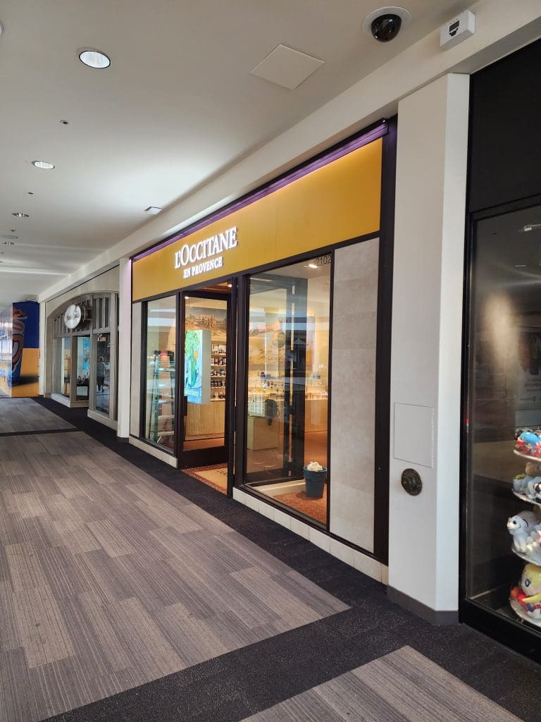 The storefront of L'Occitane en Provence at Brea Mall features glass doors and bright interior lighting, creating a refreshing ambiance as it nestles between other retail stores.