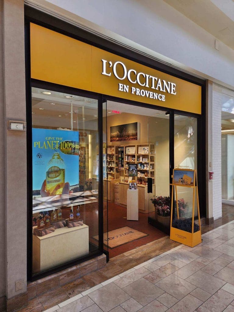 The storefront of L'Occitane en Provence at Chestnut Mall features a glass display showcasing products and a refreshing promotional poster on the left.