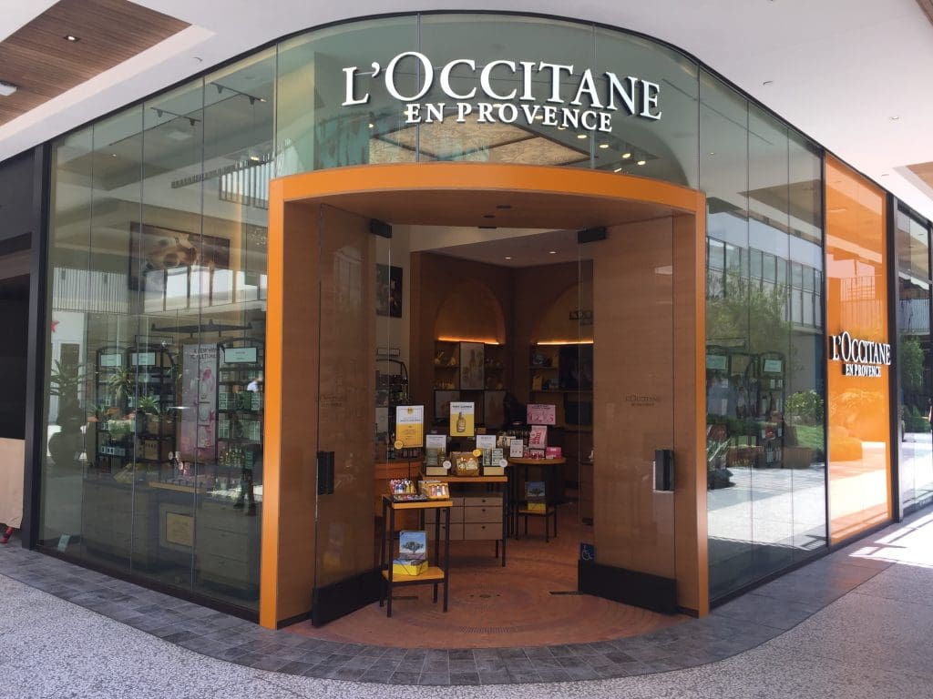 The storefront of L'Occitane en Provence at Century City Mall features glass windows and an inviting orange archway, showcasing a delightful array of products inside.
