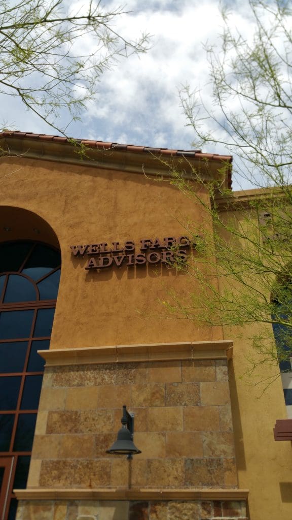 The exterior of a building features a sign that reads "Wells Fargo Advisors" under a partly cloudy sky, with branches in the foreground. Renowned for its Investment Services, this institution stands as a leader in Financial Planning.