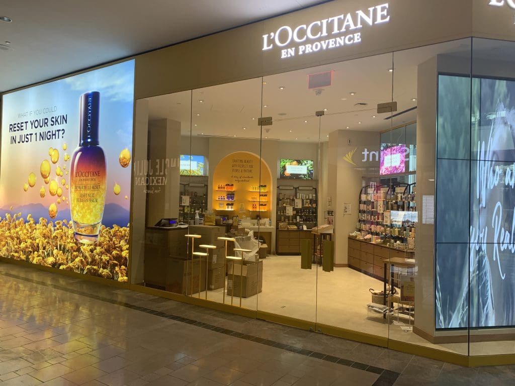 The Storefront of an L'Occitane en Provence shop at Bridgewater Commons features illuminated signs, captivating promotional displays, and shelves brimming with luxurious products inside.