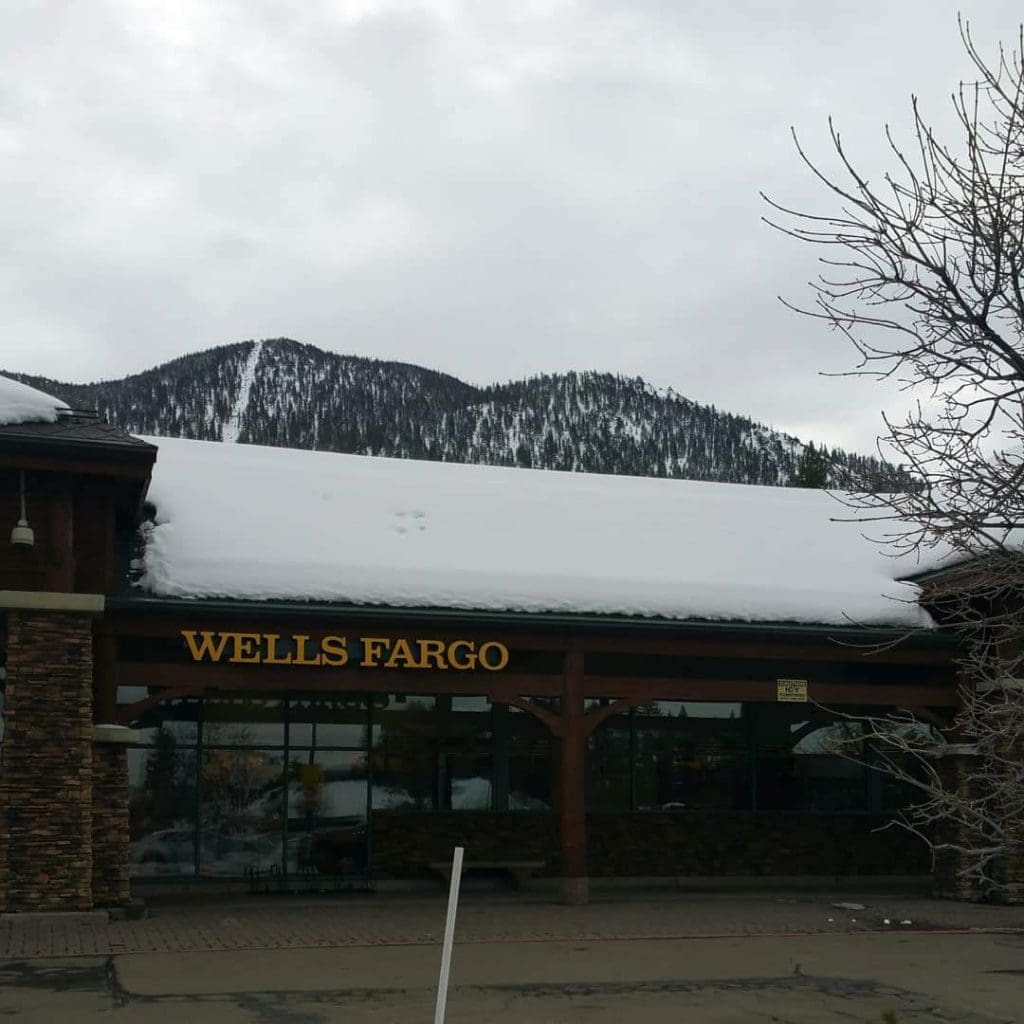 Against a backdrop of snow-capped mountains and an overcast sky, the Wells Fargo branch with a remodeled snowy roof stands prominently, echoing the pristine beauty of its surroundings.