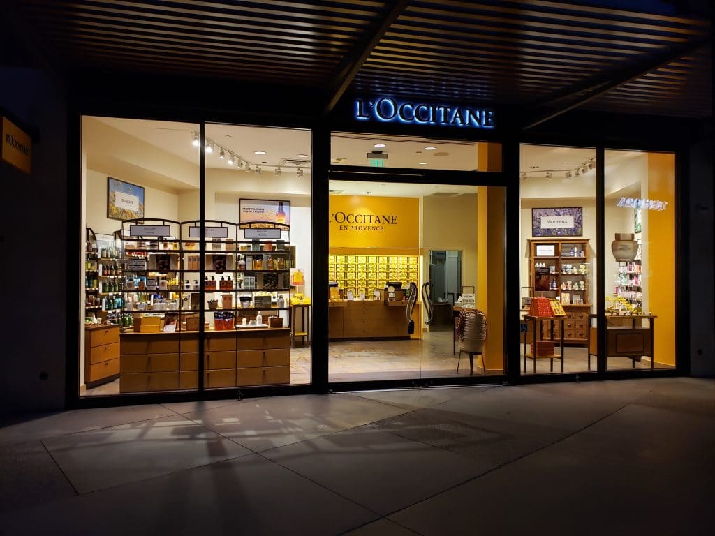 The storefront of L'Occitane en Provence at Valenia Town Center glows invitingly at night, showcasing an illuminated interior where carefully curated shelves display an array of beauty and skincare treasures. It's a pop-up paradise for those seeking luxurious self-care experiences.