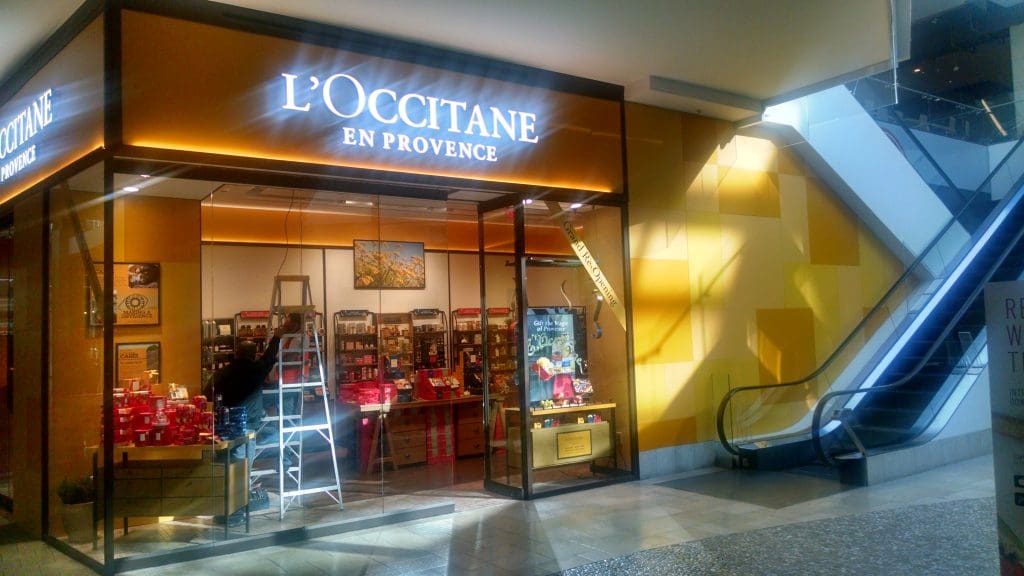 The storefront of L'Occitane en Provence, with a ladder set up in front, is located next to an escalator in the Westfield Topanga shopping mall in Los Angeles.