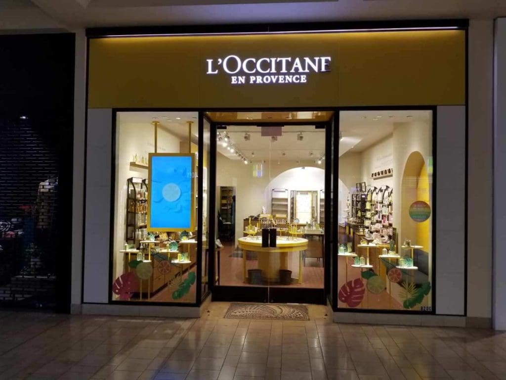 The storefront of L'Occitane en Provence in Mission Viejo features a striking yellow and black sign, large glass windows, and enticing displays of products inside, offering a delightful shopping experience.