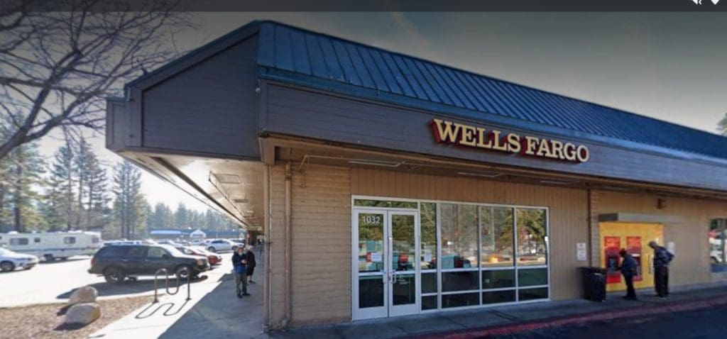 A Wells Fargo bank branch stands with a sloped roof and glass doors, part of a recent REFRESH PROJECT. A few people gather nearby while cars are parked in the background, enhancing its SEO appeal through strategic keywords.