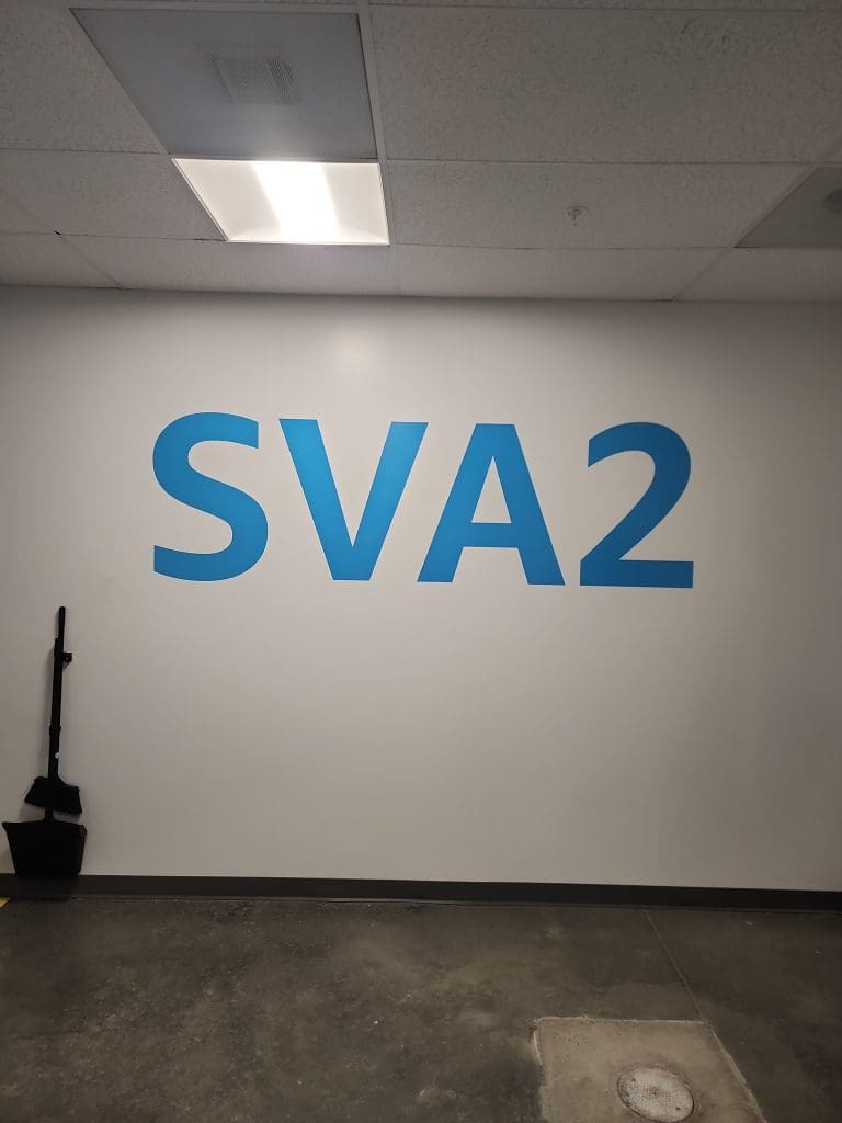 In an indoor space, a wall adorned with large blue text "SVA2" stands prominently beside cleaning equipment, lending a touch of modernity that's reminiscent of an Amazon SSD Program facility.