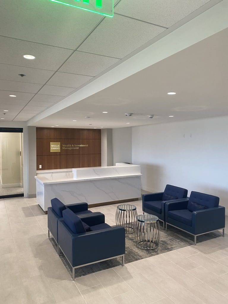 The office project features a reception area with a white desk, four blue chairs, two round tables, and a wall sign reading "Wells Fargo Wealth & Investment," highlighting the welcoming space where you can meet your wealth advisor.