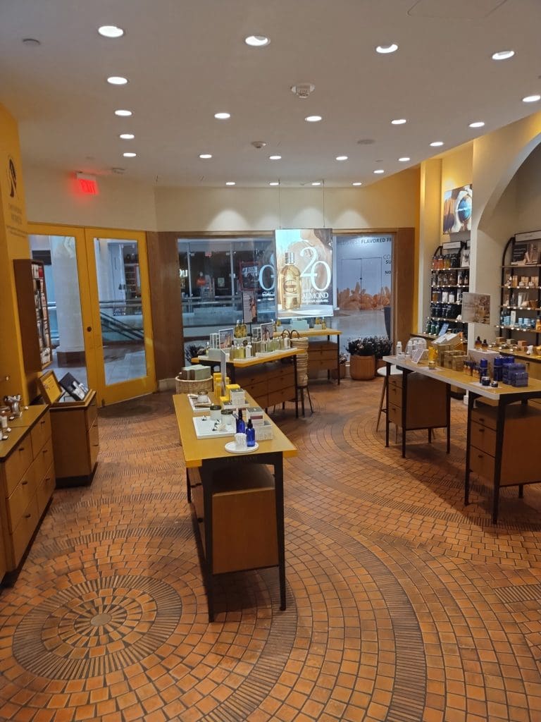 A well-lit cosmetics store interior in Stonestown features wooden display tables showcasing various skincare products and bottles, set against a backdrop of large windows and shelves, reminiscent of a chic galleria.