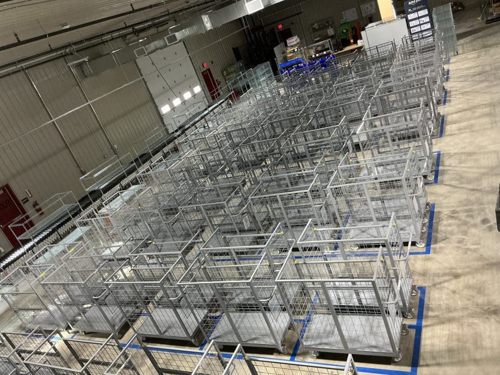 Rows of empty metal cages are neatly arranged in a large industrial warehouse with a concrete floor and high ceiling, awaiting their role in the rural program designed to support local initiatives.