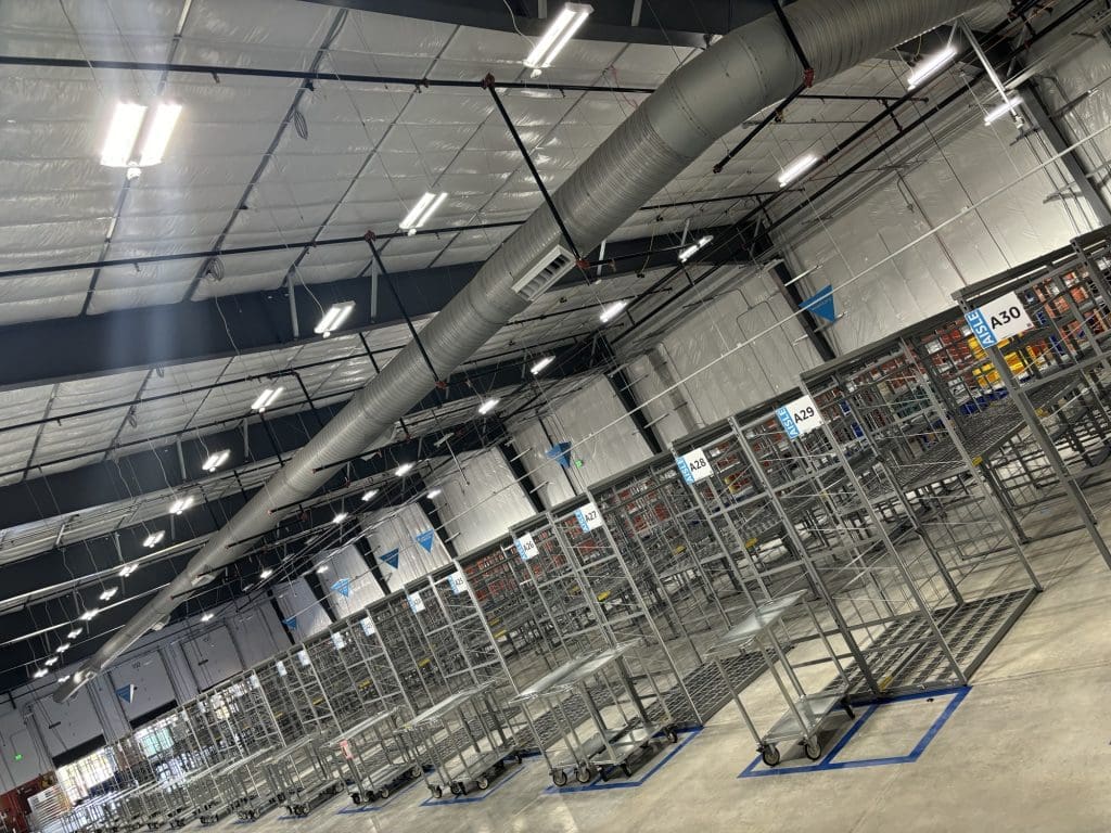 Empty metal storage racks line the expansive, well-lit warehouse with a high ceiling and exposed ventilation ducts—part of the innovative Rural Development initiative.