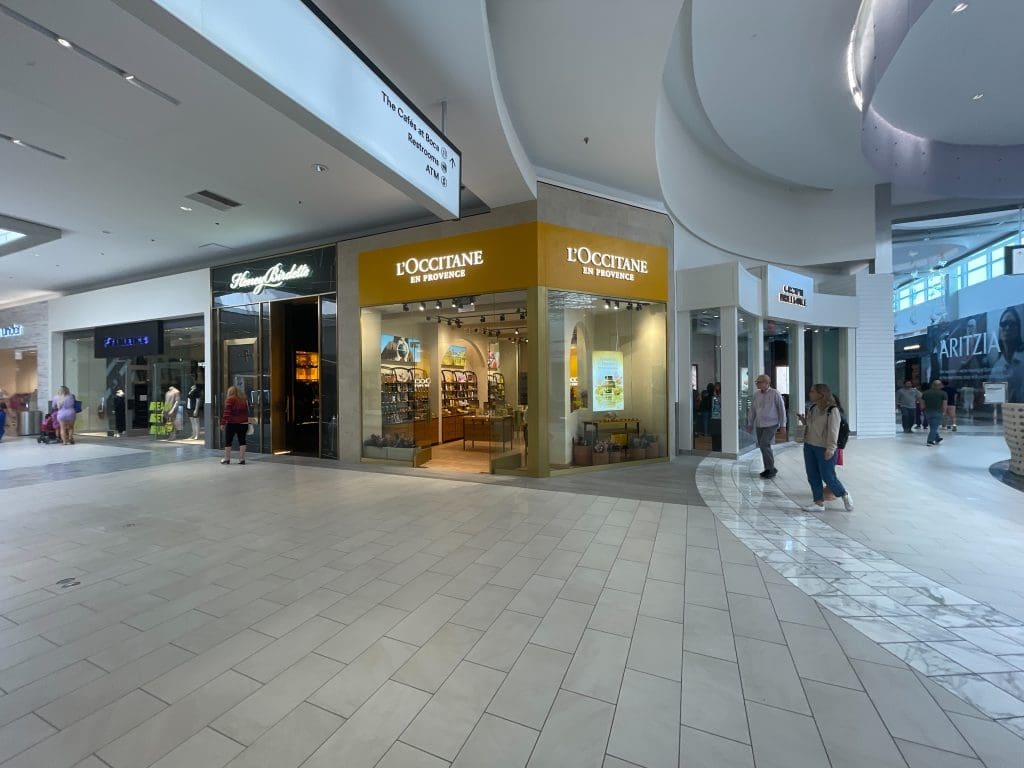 Shoppers stroll through the bustling corridor of Towne Center in Boca Raton, with a L'Occitane en Provence store on the right and an array of other enticing shops nearby.