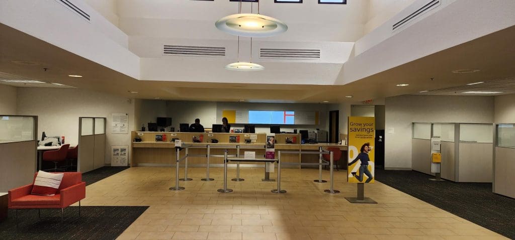 The interior of the Ocotillo Branch features teller counters, queue barriers, a cozy waiting area with red chairs, and posters promoting savings. Clients can also inquire about our exclusive Advisor Office Program for personalized financial guidance.
