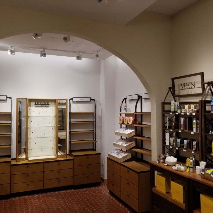 The store interior in Mission Viejo features wooden shelves and cabinets, some stocked with various products. An arched doorway leads to an adjacent room with additional displays and merchandise, reflecting the charm of local shops.