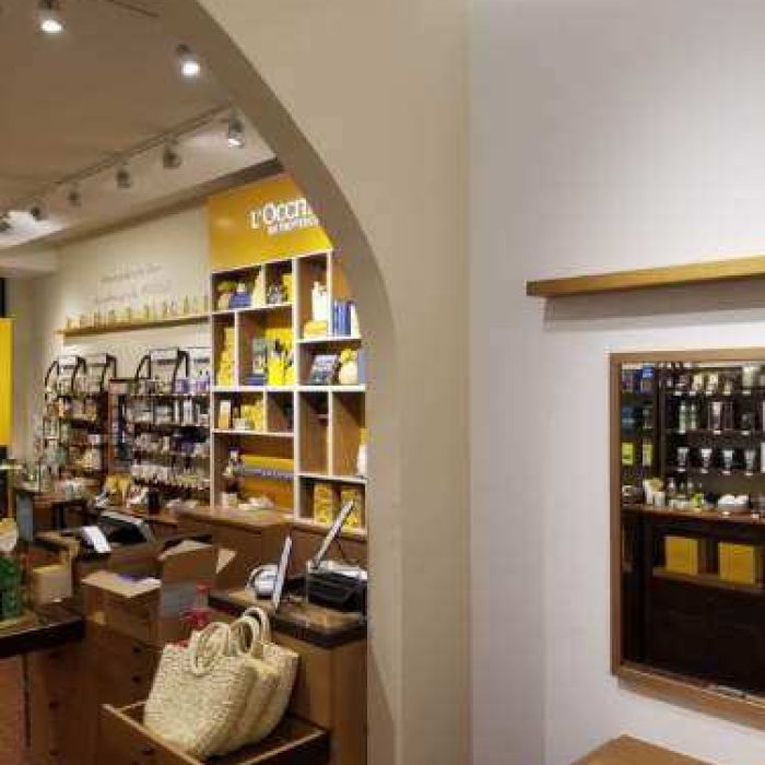 The Mission Viejo store interior features wooden shelves displaying various products. Cardboard boxes and a woven basket adorn the counter. Warm lighting highlights the organized merchandise, creating an inviting ambiance typical of charming local shops.