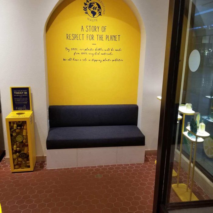 A cozy seating area in Mission Viejo with a yellow wall features a sign about respecting the planet, alongside a bin filled with small yellow capsules, creating an inviting space perfectly suited for exploring nearby shops.